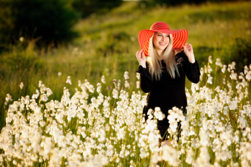 blond woman in flower field posing with red hat.