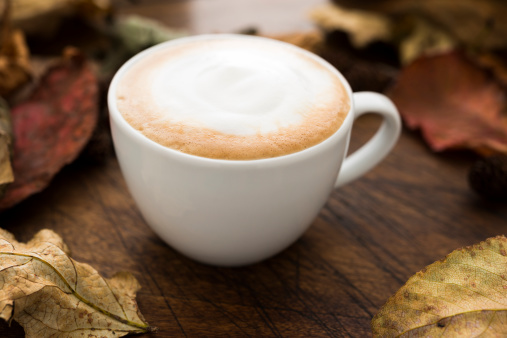 Cappuccino Coffee on an aged wood background surrounded by dried Autumn Leaves.
