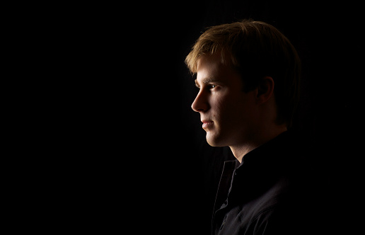 Low Key portrait of a young man against a black background. Dark relaxed profile shot with black copy space.