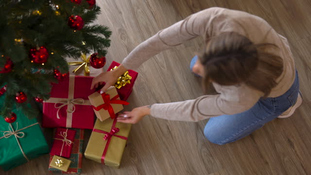 Latin American woman placing a present under the Christmas tree with other presents