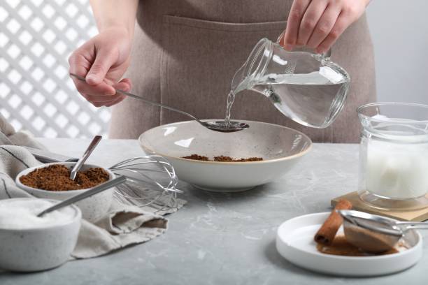 istock Making dalgona coffee. Woman pouring water into bowl at light gray table, closeup 1713753542