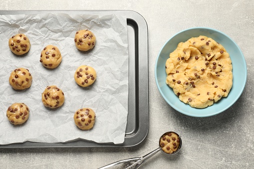 Bowl with dough and uncooked chocolate chip cookies on light grey table, flat lay