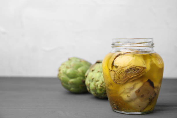 Pickled and fresh artichokes on grey wooden table. Space for text