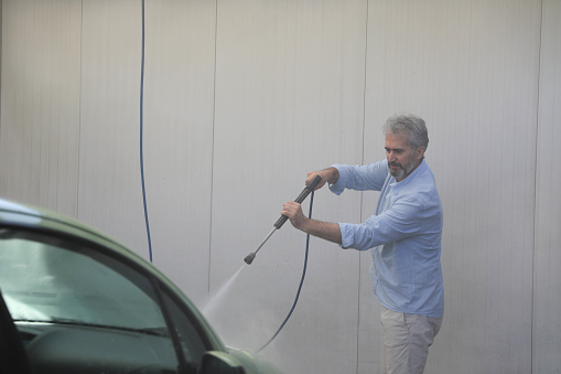Senior man power washing his car in a self service car wash during the day.