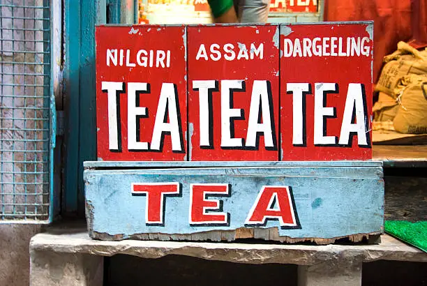 Different blends of tea in containers outside an indian tea shop. The blend names of the tea; nilgiri, assam and darjeeling are painted on the red containers.