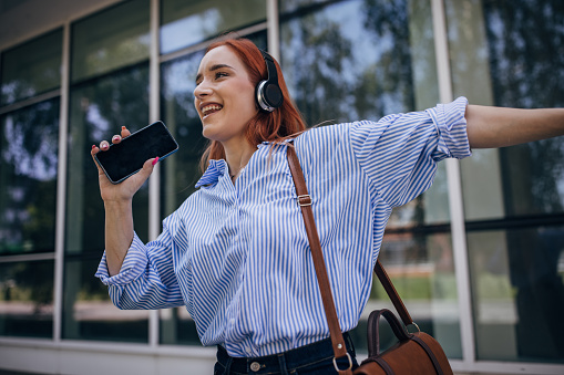 One woman, modern businesswoman with headphones singing on the street.