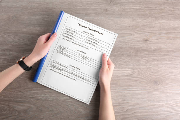 Woman holding complaint form at wooden table, top view