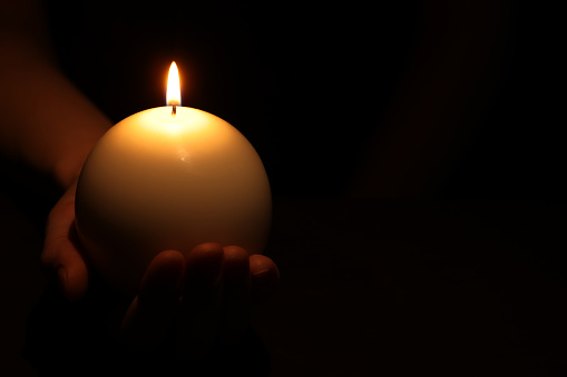 Woman holding burning candle in hand on black background, closeup. Space for text