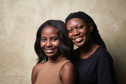 Two African American women together looking at camera and smiling in a studio shot