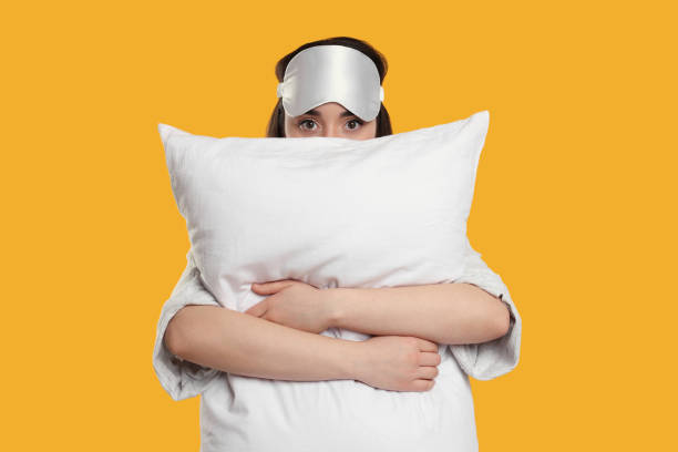 istock Tired young woman with sleep mask and pillow on yellow background. Insomnia problem 1713783394