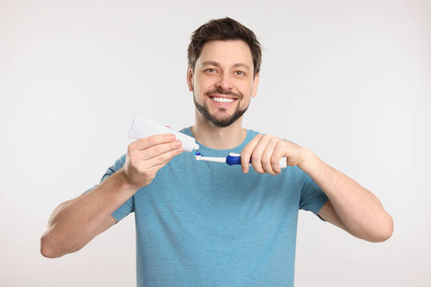 istock Happy man squeezing toothpaste from tube onto toothbrush on white background 1713790862