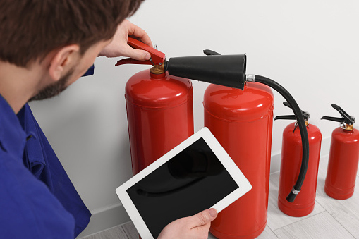 Man with tablet checking fire extinguishers indoors, closeup