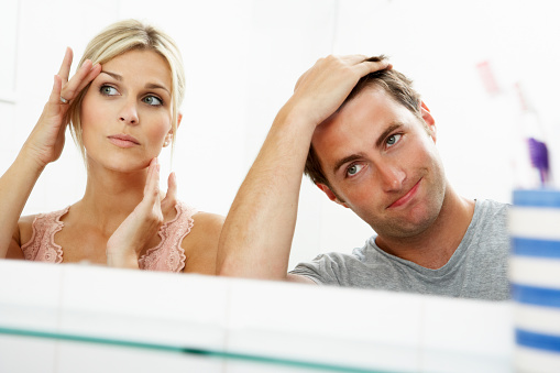 Couple Looking At Reflections In Mirror For Signs Of Ageing In Bathroom