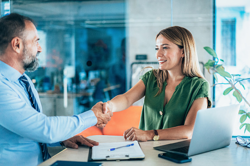 Business people shaking hands in the office. Two entrepreneurs on meeting in board room. HR manager  meet and greet new employee on job interview. Cheerful Businessman and businesswoman greeting each other for successful partnership. Signing new agreement in modern office