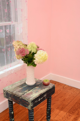 Freshly picked hydrangeas and sedum decorate a table in a room with pastel pink walls.