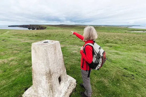 Ultra wide angle view of the north and east coasts of the United Kingdom from the triangulation pillar on Duncansby Head beside John o'Groats in Scotland. The female hiker is pointing towards the Duncansby Stacks along the east coast.