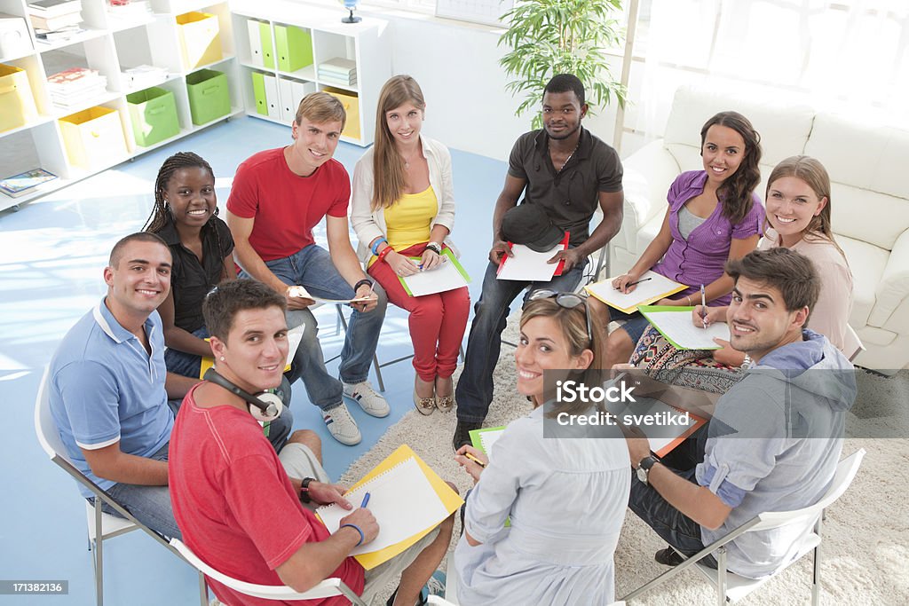 Group of students sitting in a circle. "Large group of students or young people sitting in a circle with copybooks, having discussion together. Looking at camera.See more STUDENTS or YOUNG PEOPLE TOGETHER images ISOLATED on white or INDOORS. Click on image below for lightbox." Large Group Of People Stock Photo