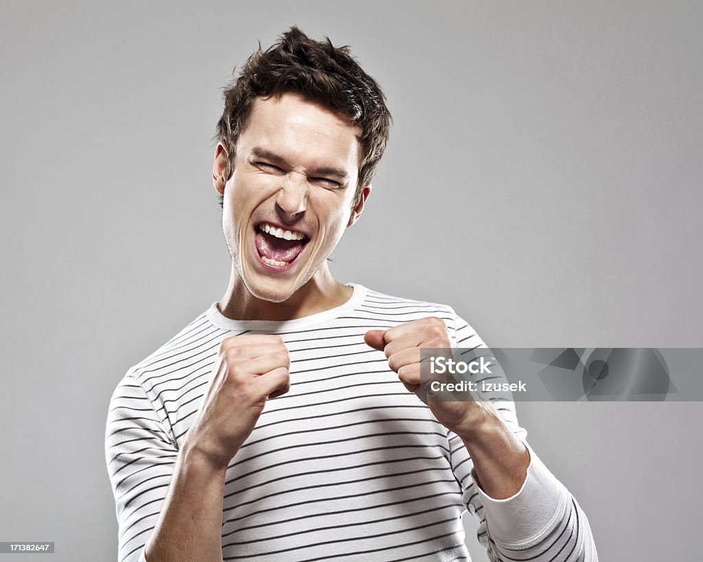 Winner "Portrait of excited young man, raising his fists and screaming with eyes closed. Studio shot, grey background." Men Stock Photo
