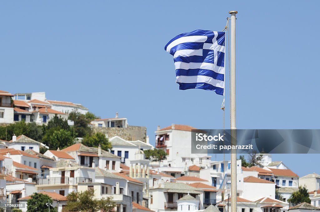 Greek flag swinging on a post Greek flag swinging on a post with a typical small town in the background Backgrounds Stock Photo