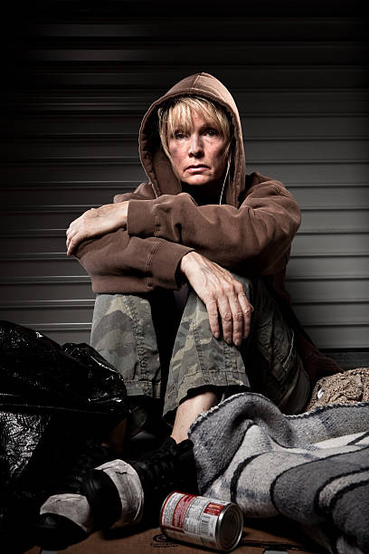 Homeless woman sitting on the ground in dramatic lighting.