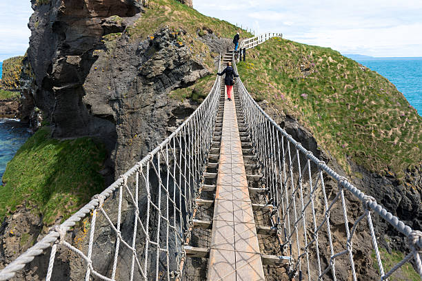 Carrick-a-Rede Rope Bridge Two people crossing the Carrick-a-Rede Rope Bridge, a popular tourist destination in Northern Ireland. northern ireland photos stock pictures, royalty-free photos & images