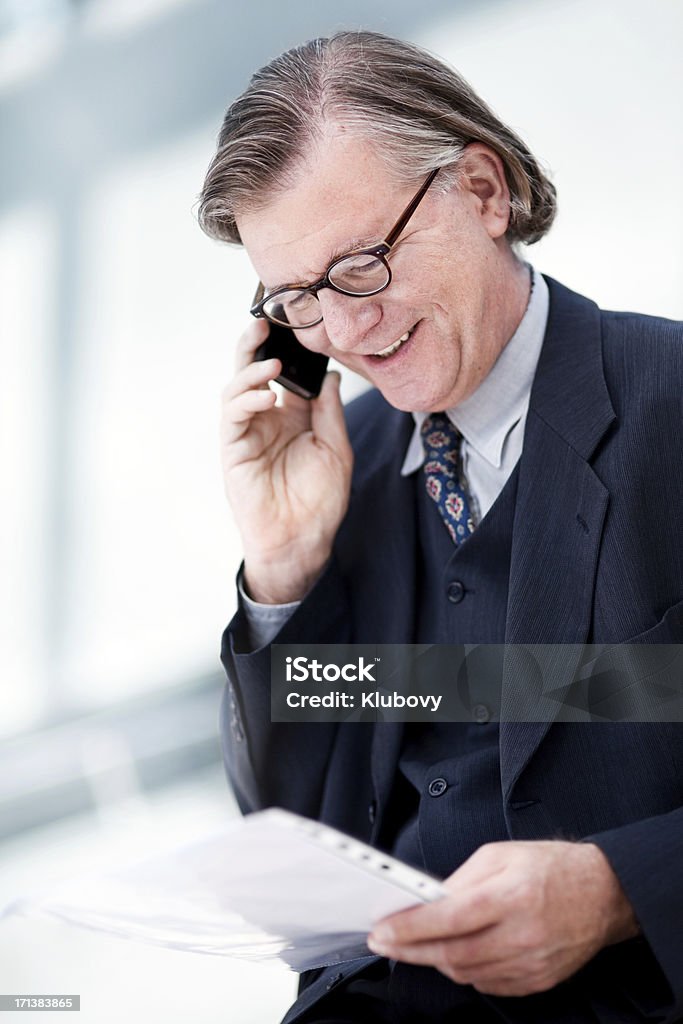 Businessman talking on the phone Photo of a businessman talking on the phone, looking at papers. Shallow depth of field, contemporary architecture in the background. 50-59 Years Stock Photo