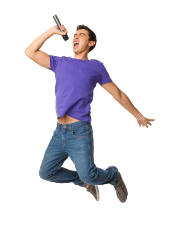 Lively young boy in casual wear singing into microphone in mid-air. Vertical shot. Isolated on white.