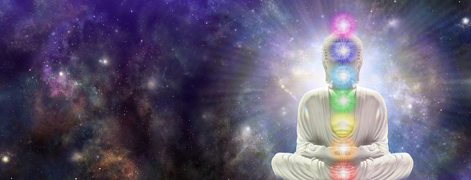buddha on right side with seven chakras against a starry dark blue celestial sky with a massive nebula and copy space for text