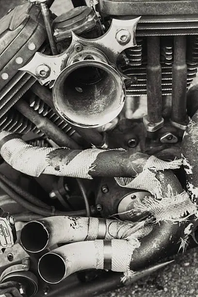 A ratty motorcycle intake and exhaust with tattered heat wrap.  Toned black and white.