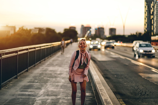woman smiling and standing on city bridge against backdrop of sunset