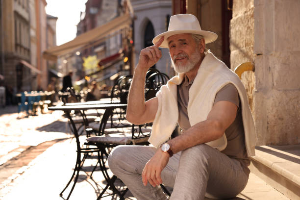 Handsome senior man sitting on doorstep outdoors, space for text