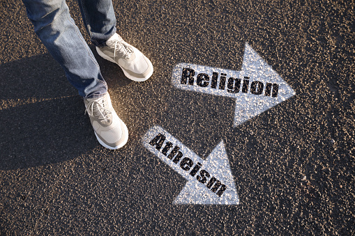 Choice between atheism and religion. Man standing near drawn marks on road, closeup. White arrows pointing in different directions