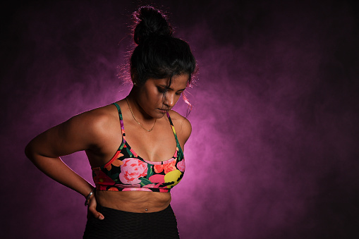 Waist up image of a young woman dressed in active wear, mid work out. Pink background.