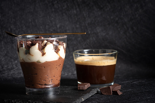 Tiramisu creamy cake dessert in a glass cup with mint leaves and coffee cup on black wooden background