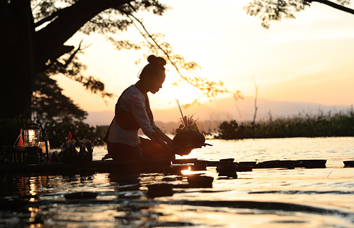 A beautiful Asian woman floats a leaf basket called Krathong in Thai to pray respect to the Goddess of Water at the river on the full moon day of November