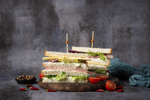 Sandwich with ham, cheese, tomato, lettuce, chicken meat, white bread and glass of beer on black -gray background