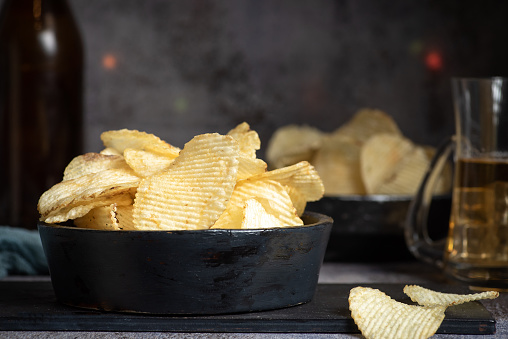Potato chips. Chips in a black bowl on a black background. Good for a snack with a beer. Good for advertising beer festivals, pubs, restaurants. Food and drink photography. High resolution macro photo