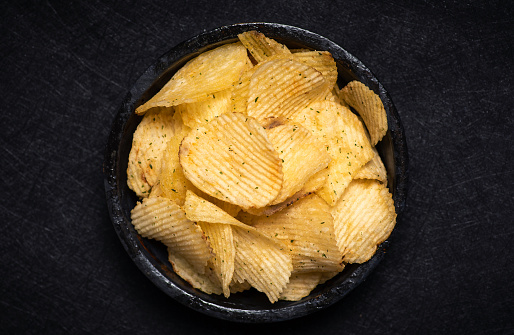 Close up of potato chips in a black bowl on a black background