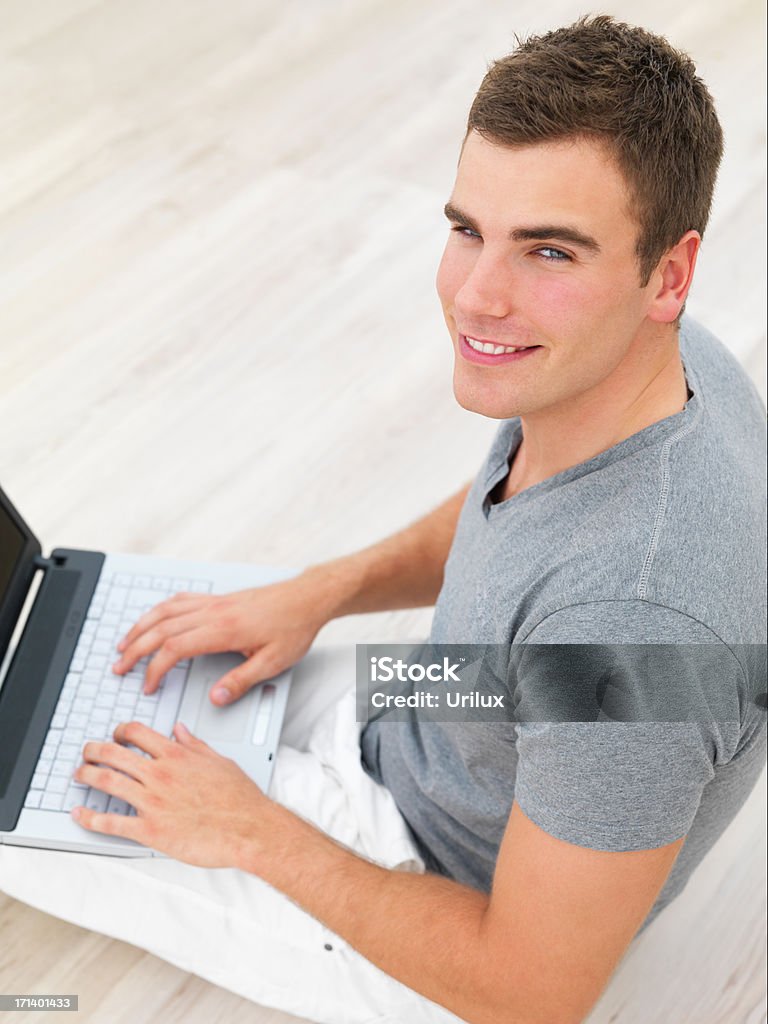Souriant jeune homme assis sur le sol à l'aide d'un ordinateur portable - Photo de Adulte libre de droits