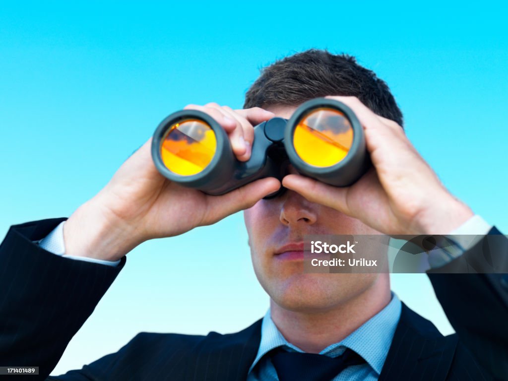 Joven mirando a través de un hombre de negocios aislado sobre cielo azul binocular - Foto de stock de Adulto libre de derechos