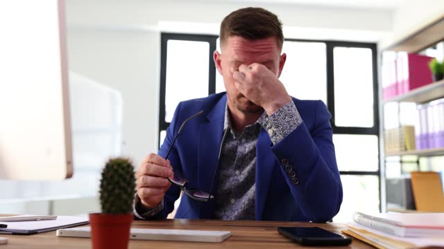 Tired exhausted businessman massages bridge of nose, takes off glasses at workplace