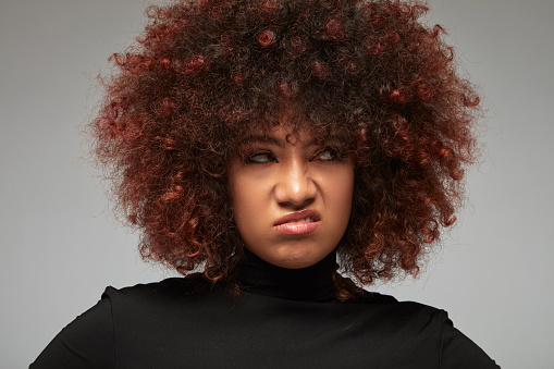 A mixed race young woman with curly hair, resentful and angry.