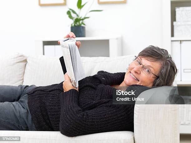 Szczęśliwy Dojrzała Kobieta Leżąc Na Kanapie Czytanie Książki - zdjęcia stockowe i więcej obrazów Czytać