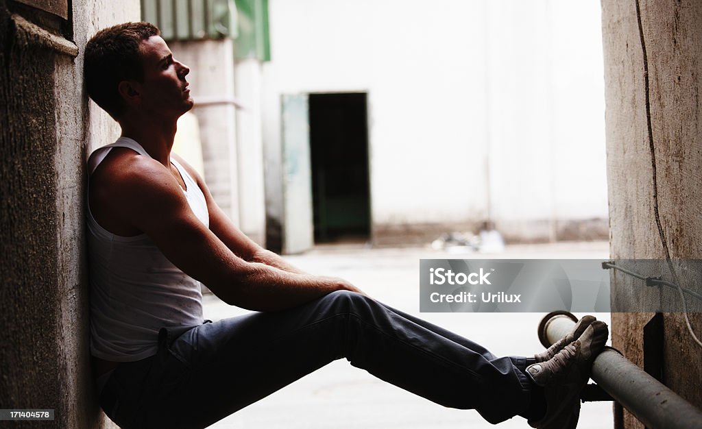 Giovane uomo seduto sulla pavimentazione in un vicolo volontà. - Foto stock royalty-free di Adulto