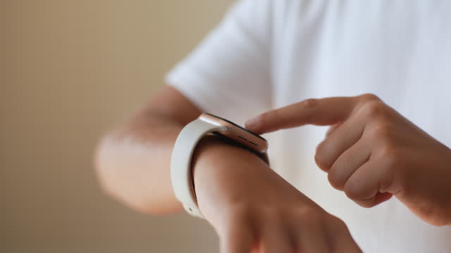 Close-up cropped shot of unrecognizable little preteen girl using modern smart watch touching button and touchscreen while posing indoors