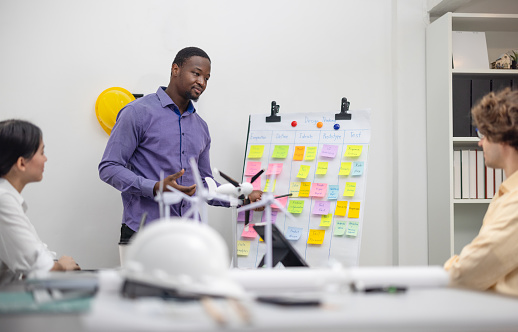 A diverse startup team develop, collaborates on a powerful, lightweight, portable wind turbine prototype, aligning with potential user demand and renewable energy needs to secure investor funding.