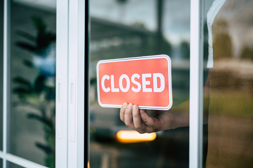 A retail store owner in a coffee shop is seen turning the closed sign on the door's glass surface. The widespread closures of stores, and restaurants during the COVID-19 lockdown and quarantine period