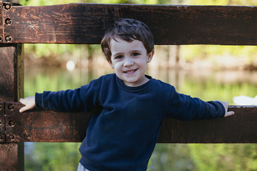 3-year-old boy with blond hair, leaning on a railing at a lakeside park