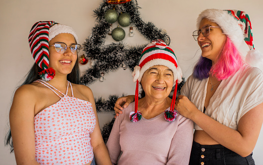 a grandmother and two young women together wearing christmas hats and smiling