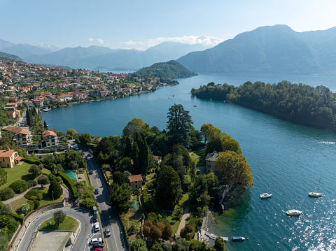 Aerial view over the small town of Ossuccio and the Isola Comacina on the shores of Lake Como in Italy. Lake Como is an Iconic lake destination known for its scenic beauty, mountain vistas & historic lakeside residences.